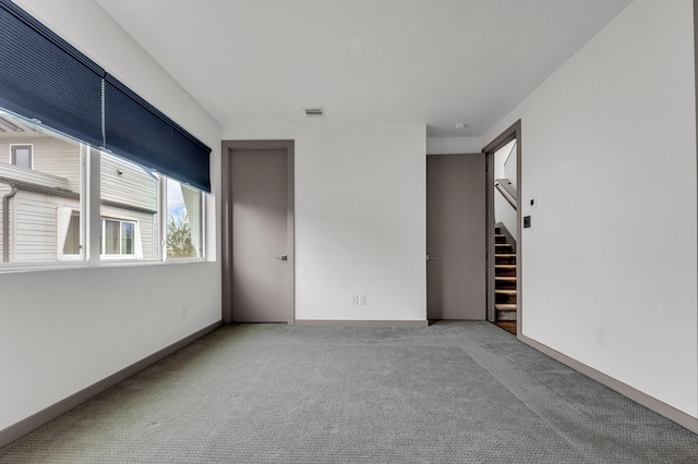 carpeted spare room with stairway, baseboards, and visible vents