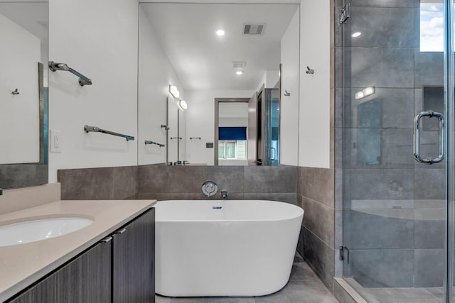 bathroom with visible vents, a freestanding bath, vanity, a stall shower, and tile walls