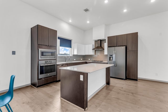 kitchen with visible vents, a sink, a center island, appliances with stainless steel finishes, and wall chimney range hood