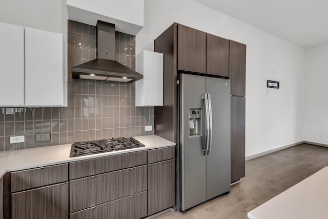 kitchen with light wood finished floors, stainless steel fridge with ice dispenser, gas stovetop, light countertops, and wall chimney exhaust hood