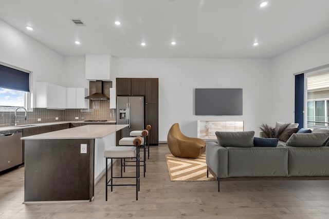 kitchen with a breakfast bar, a sink, stainless steel appliances, wall chimney exhaust hood, and a center island