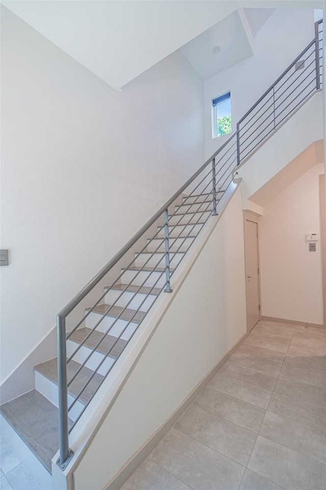 stairway with tile patterned floors, a high ceiling, and baseboards