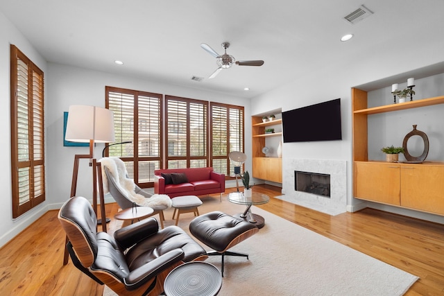 living room featuring built in features, light wood-type flooring, a fireplace with flush hearth, and visible vents