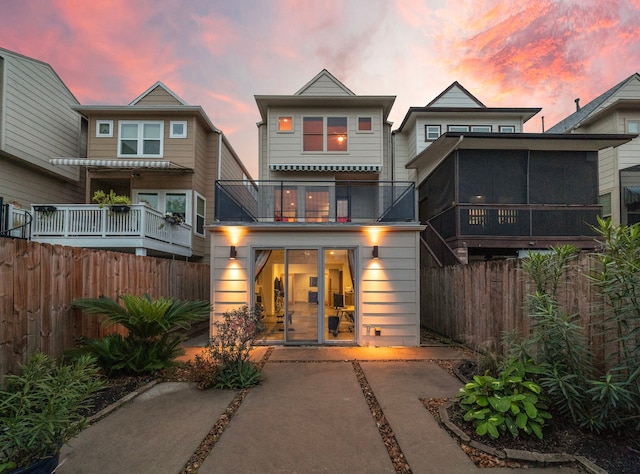 back of house at dusk featuring a balcony and fence