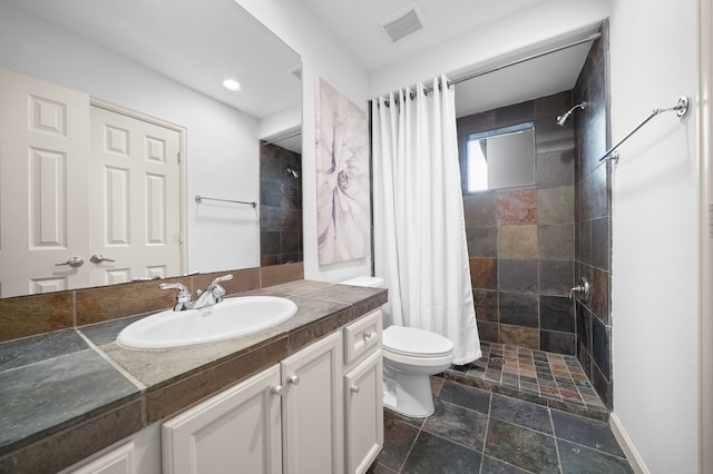 full bathroom featuring visible vents, toilet, a tile shower, stone tile floors, and vanity