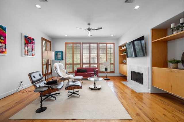 living area featuring built in shelves, baseboards, recessed lighting, a fireplace, and light wood-type flooring