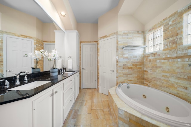 full bathroom featuring double vanity, a whirlpool tub, vaulted ceiling, and a sink