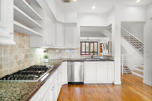 kitchen with a sink, open shelves, tasteful backsplash, stainless steel appliances, and light wood-style floors