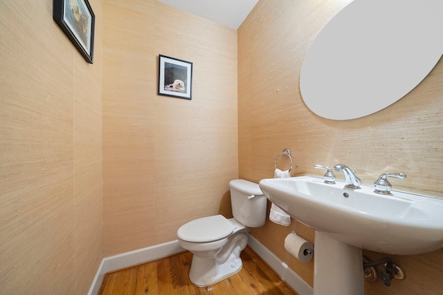 half bath with toilet, baseboards, and wood finished floors