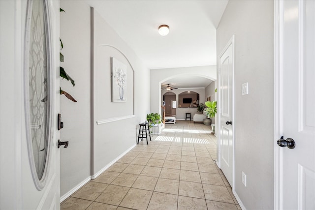 hallway featuring arched walkways, light tile patterned floors, and baseboards