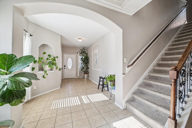 tiled foyer entrance with baseboards, arched walkways, and stairs