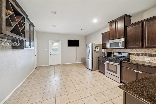 kitchen featuring dark stone countertops, light tile patterned floors, stainless steel appliances, decorative backsplash, and dark brown cabinets