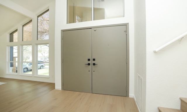 foyer entrance featuring visible vents, light wood-style floors, and a towering ceiling