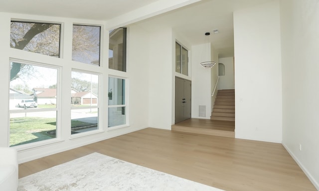 unfurnished room featuring light wood-type flooring, visible vents, a towering ceiling, and stairway