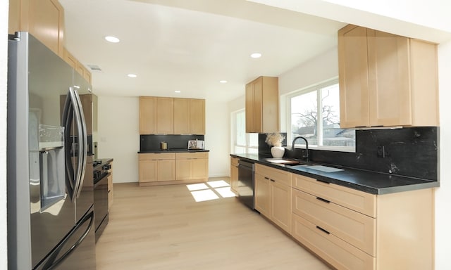 kitchen with light wood-style flooring, a sink, light brown cabinetry, stainless steel appliances, and dark countertops