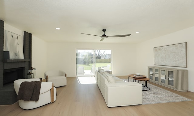 living area featuring recessed lighting, light wood-type flooring, a brick fireplace, and ceiling fan