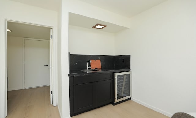 bar featuring wine cooler, baseboards, light wood finished floors, and a sink