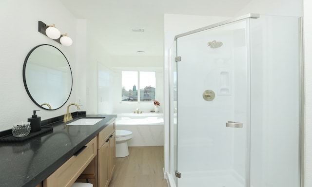 bathroom featuring a garden tub, toilet, wood finished floors, a shower stall, and vanity