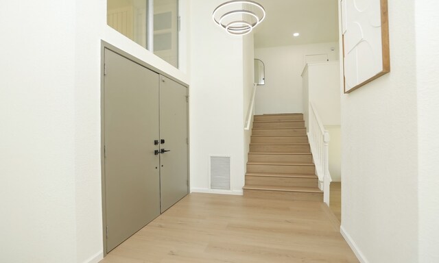 hallway with visible vents, stairway, baseboards, and light wood-style floors