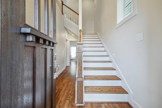 staircase featuring a high ceiling, baseboards, and wood finished floors