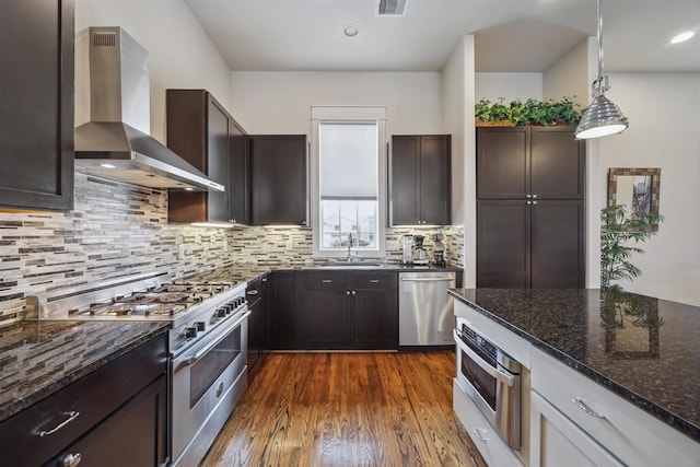 kitchen featuring dark wood finished floors, dark stone counters, wall chimney exhaust hood, and appliances with stainless steel finishes