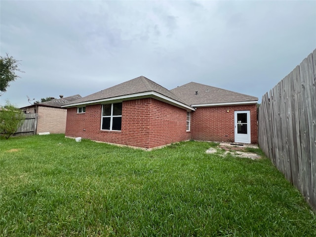 back of house with a yard, fence private yard, brick siding, and roof with shingles