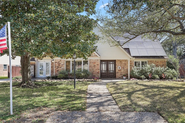 view of front of property with solar panels, a front yard, french doors, and brick siding