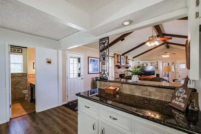 kitchen with lofted ceiling with beams, a textured ceiling, dark wood-style floors, white cabinetry, and dark stone counters