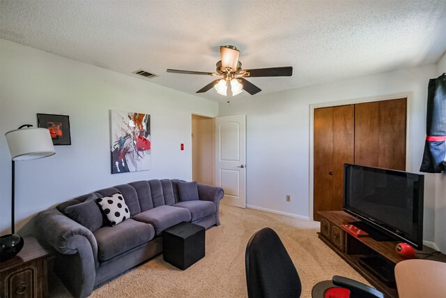 living room featuring a ceiling fan, baseboards, visible vents, a textured ceiling, and light colored carpet