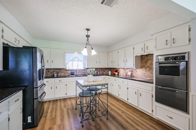 kitchen featuring wood finished floors, visible vents, stainless steel appliances, white cabinetry, and dark countertops