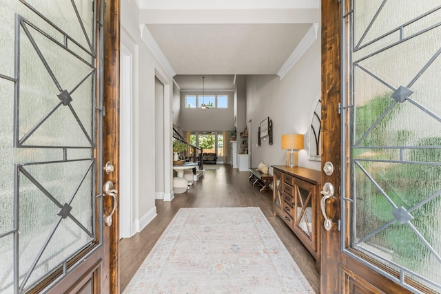 foyer with a notable chandelier, crown molding, baseboards, a towering ceiling, and dark wood-style flooring