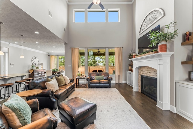 living area featuring plenty of natural light, a glass covered fireplace, dark wood finished floors, and ornamental molding