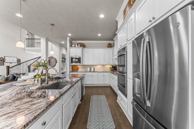 kitchen with a sink, backsplash, appliances with stainless steel finishes, white cabinetry, and dark wood-style flooring