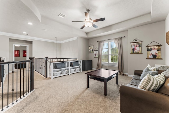 carpeted living room with visible vents, baseboards, a tray ceiling, and a ceiling fan