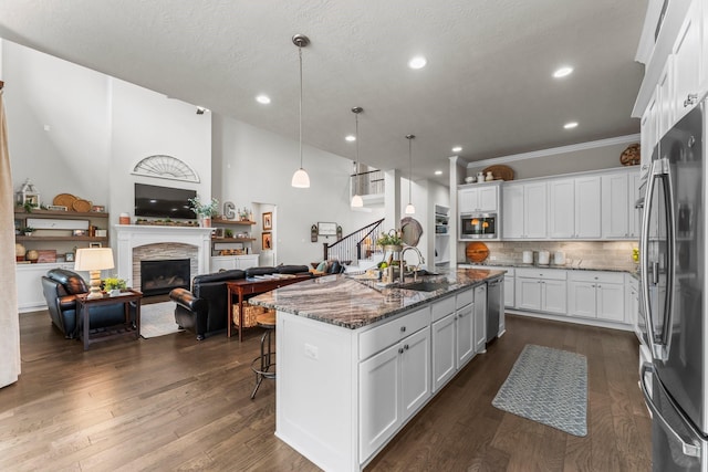 kitchen featuring a sink, dark stone countertops, dark wood-style floors, stainless steel appliances, and a stone fireplace