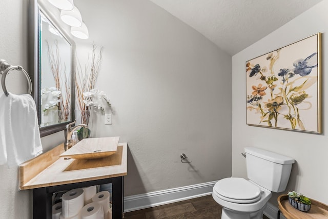 half bath with toilet, wood finished floors, baseboards, vanity, and vaulted ceiling