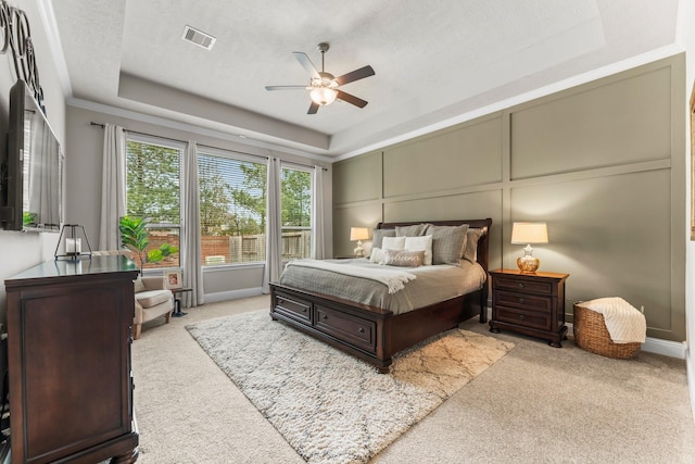 carpeted bedroom with visible vents, a raised ceiling, ceiling fan, and a decorative wall