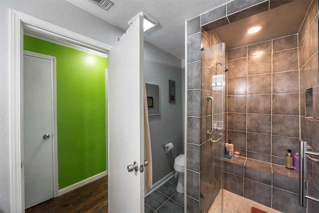 bathroom featuring visible vents, toilet, a textured ceiling, a shower stall, and baseboards