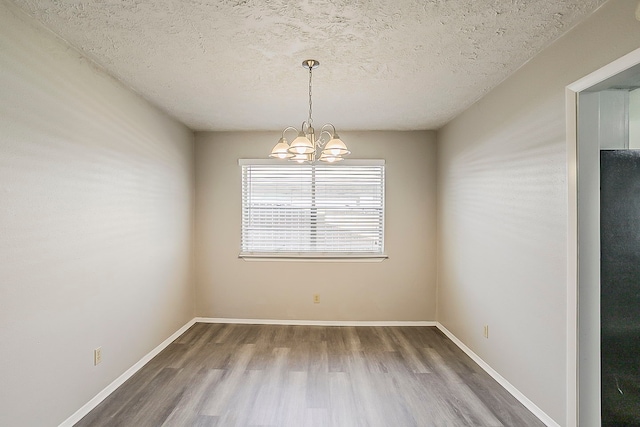 empty room with baseboards, a textured ceiling, an inviting chandelier, and wood finished floors