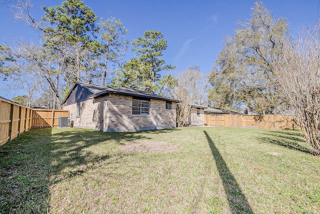 rear view of property featuring a lawn, central AC unit, a fenced backyard, and brick siding