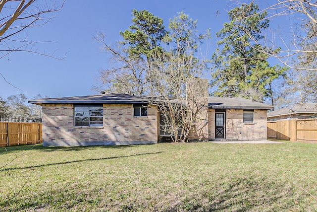 rear view of property featuring a lawn, brick siding, and a fenced backyard