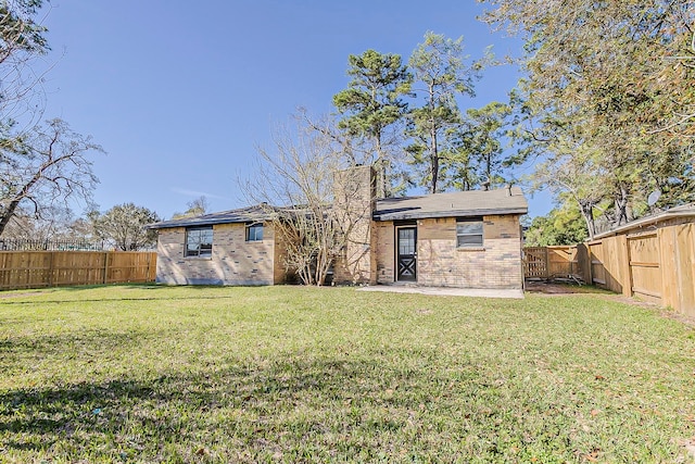 rear view of house with a lawn, brick siding, a fenced backyard, and a chimney