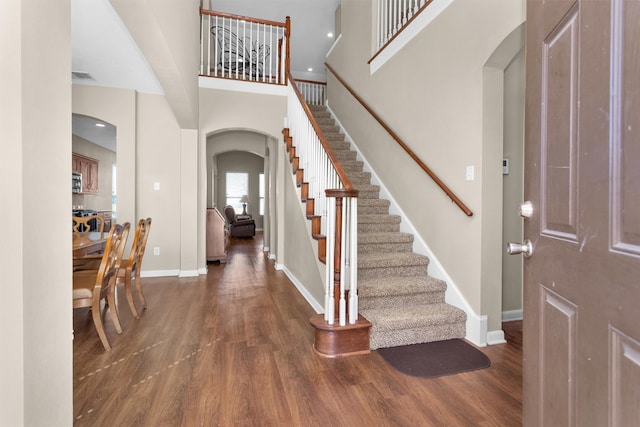 foyer with wood finished floors, stairway, arched walkways, a high ceiling, and baseboards