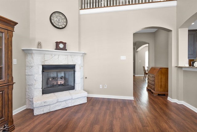 unfurnished living room featuring a stone fireplace, wood finished floors, baseboards, and arched walkways