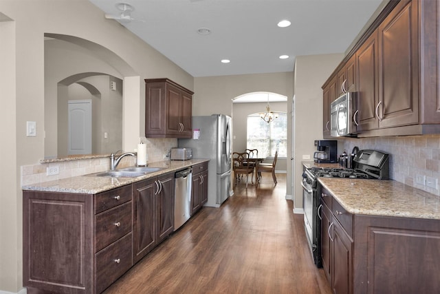 kitchen with dark wood-style floors, appliances with stainless steel finishes, arched walkways, and a sink