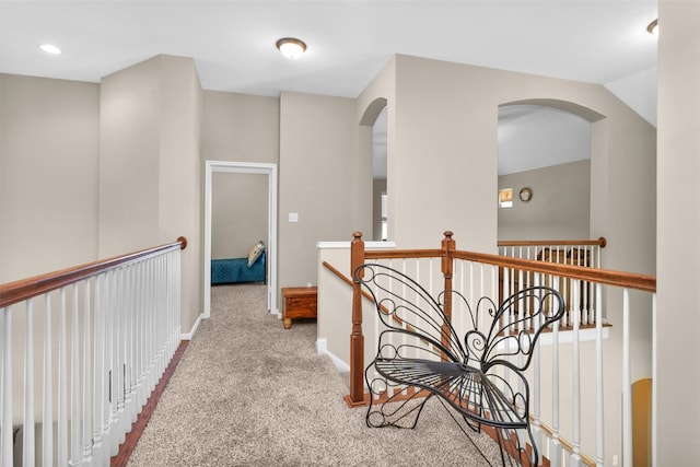 hall featuring carpet flooring, arched walkways, baseboards, and an upstairs landing