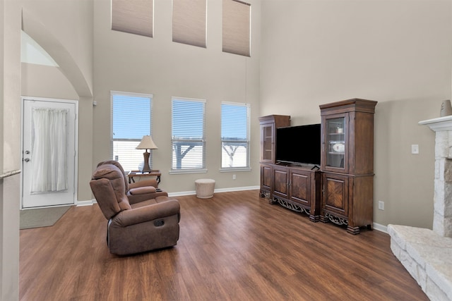 living room with a stone fireplace, dark wood-type flooring, and baseboards