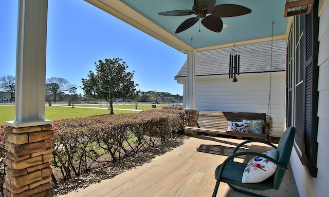 wooden terrace featuring a ceiling fan, covered porch, and a lawn