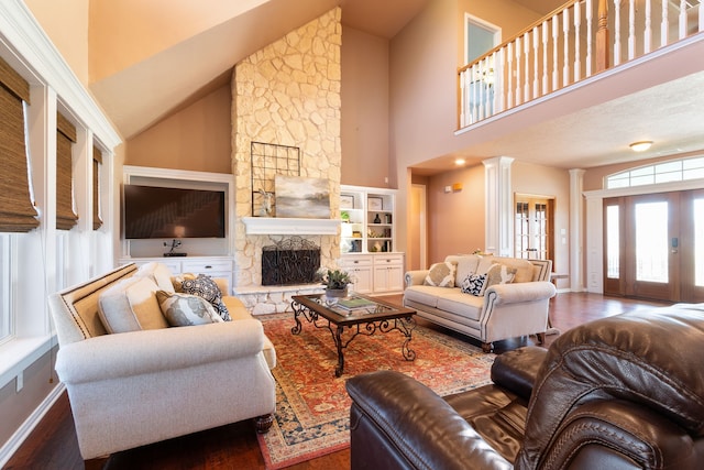 living area with baseboards, a stone fireplace, wood finished floors, and ornate columns