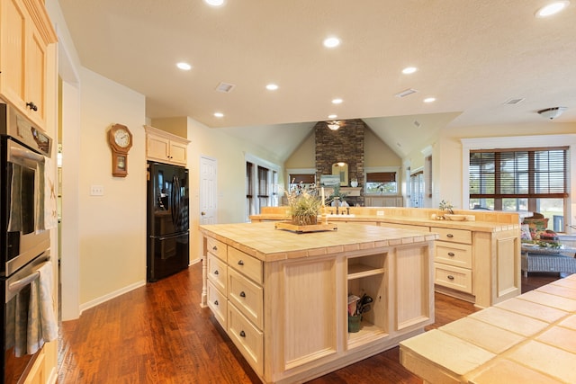 kitchen with dark wood-type flooring, an island with sink, tile countertops, lofted ceiling, and black refrigerator with ice dispenser